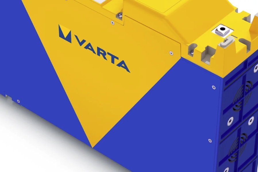 Close-up of a blue and yellow machine with the brand name VARTA, showing part of internal components and a row of rechargeable batteries.