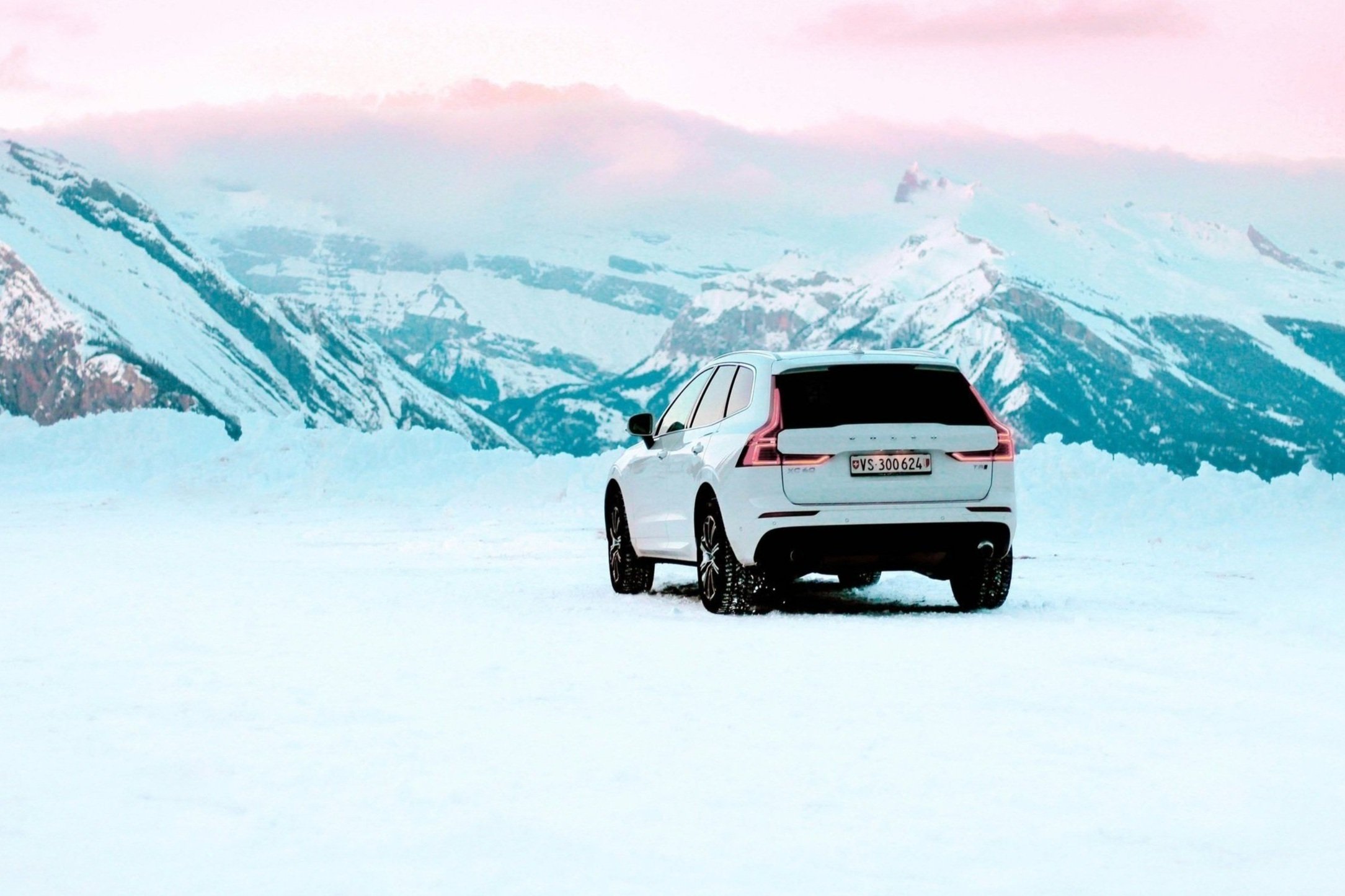 A white SUV parked on snow-covered ground with snow-covered mountains in the background.